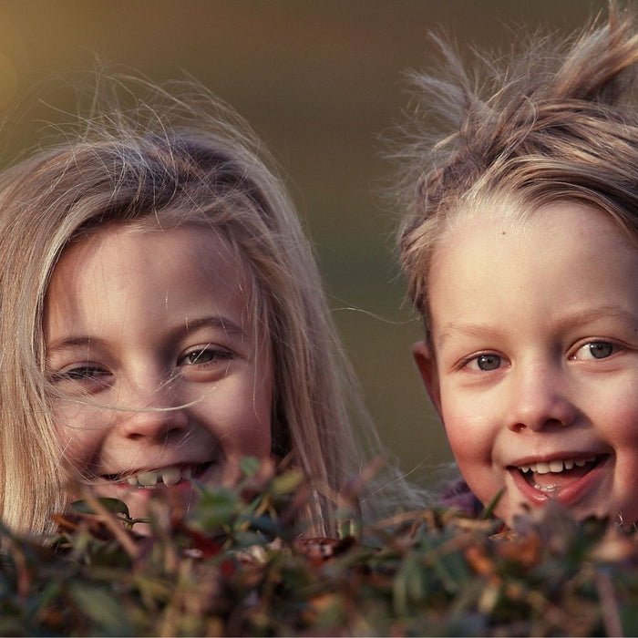 Zwei Kinder lachen in die Kamera. Sie haben Körperkontakt und können durch direkten Kopf-zu-Kopf-Kontakt Läuse übertragen. Läuseeier kann man jedoch mit einigen Hilfsmitteln erkennen. 