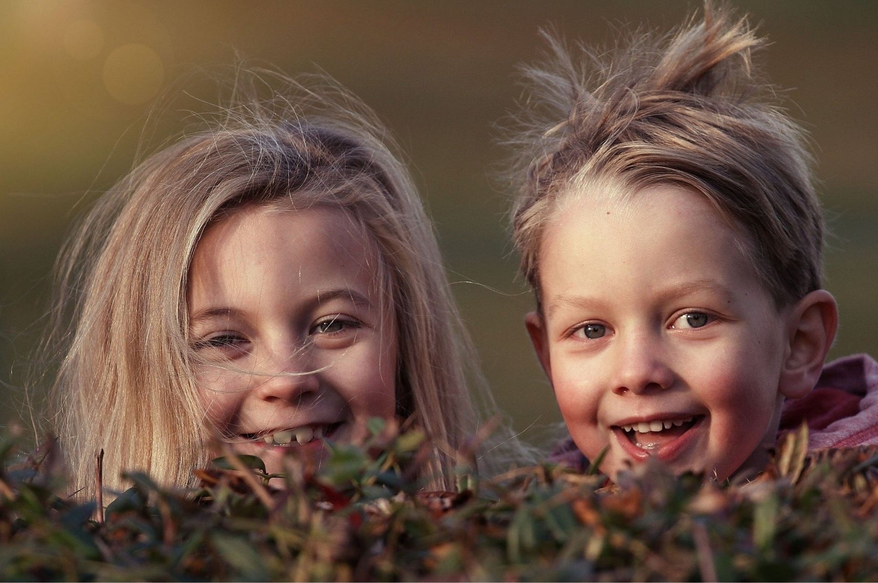 Zwei Kinder lachen in die Kamera. Sie haben Körperkontakt und können durch direkten Kopf-zu-Kopf-Kontakt Läuse übertragen. Läuseeier kann man jedoch mit einigen Hilfsmitteln erkennen. 